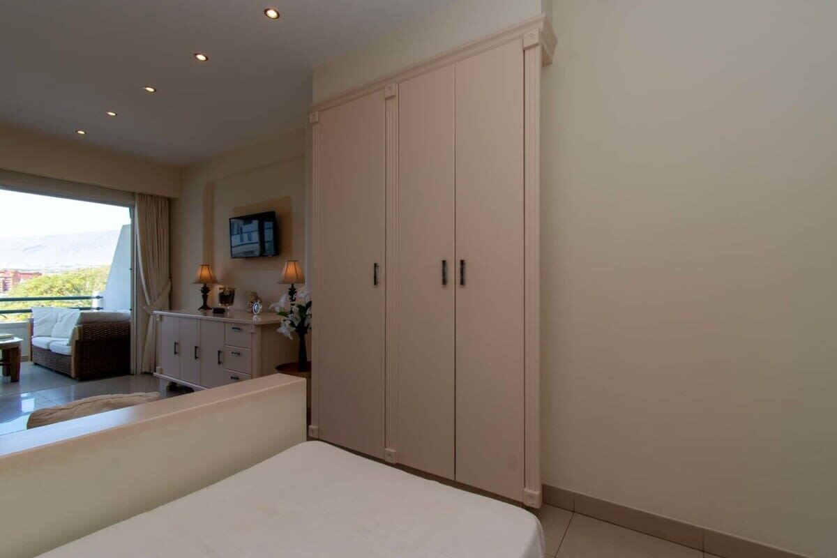 A bedroom with a bed, a wardrobe, a desk with a lamp, and a television on the wall.