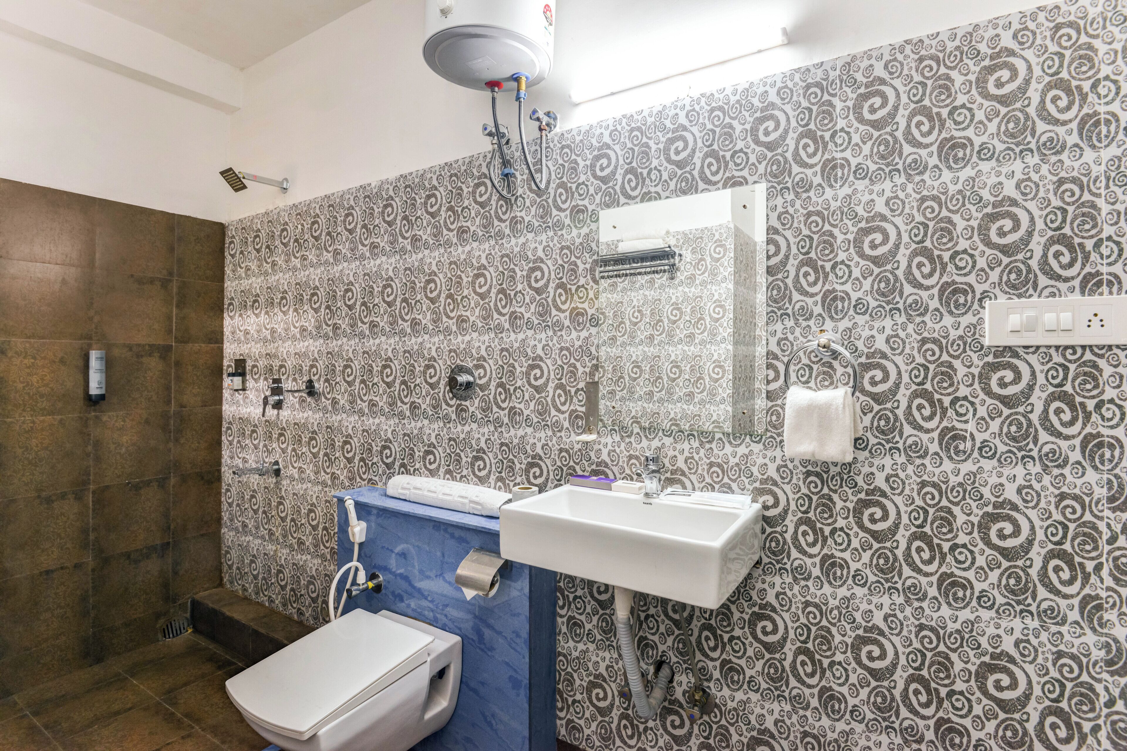 A bathroom with patterned wallpaper, a sink, a toilet, and a shower.