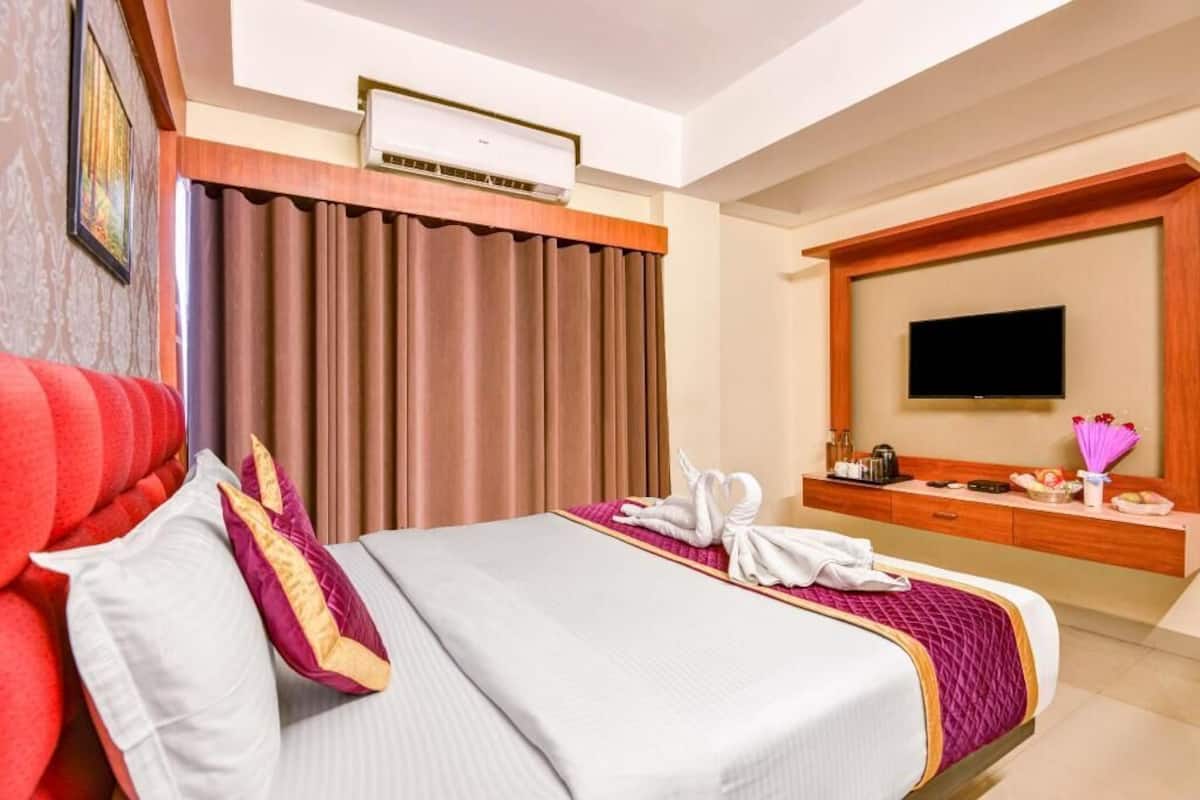 Ein Hotelzimmer mit Bett, Fernseher, Schreibtisch und einem fensterbepflanzten Fenster.