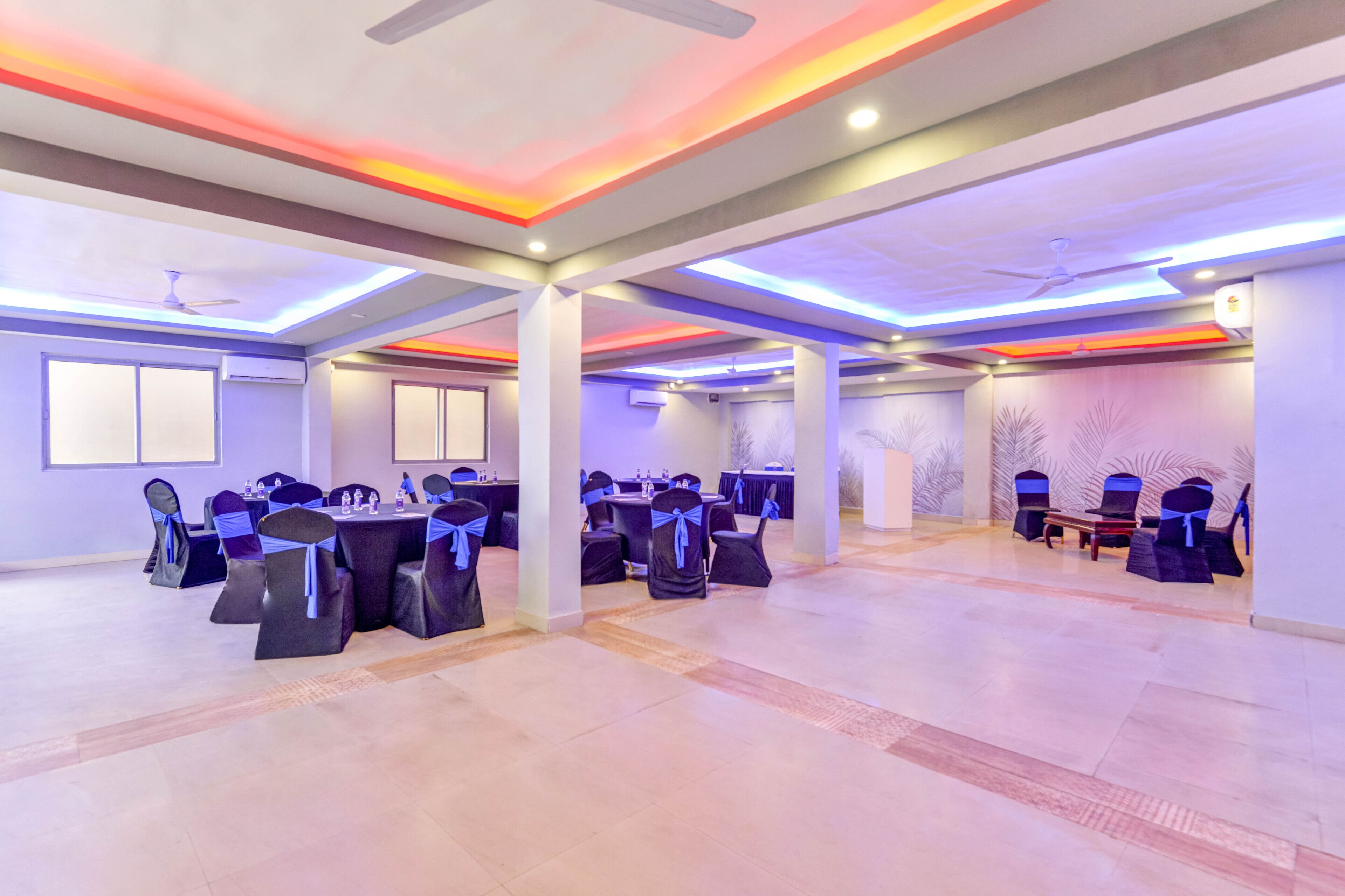 A spacious conference room with multiple tables and chairs, ceiling fans, and recessed lighting.