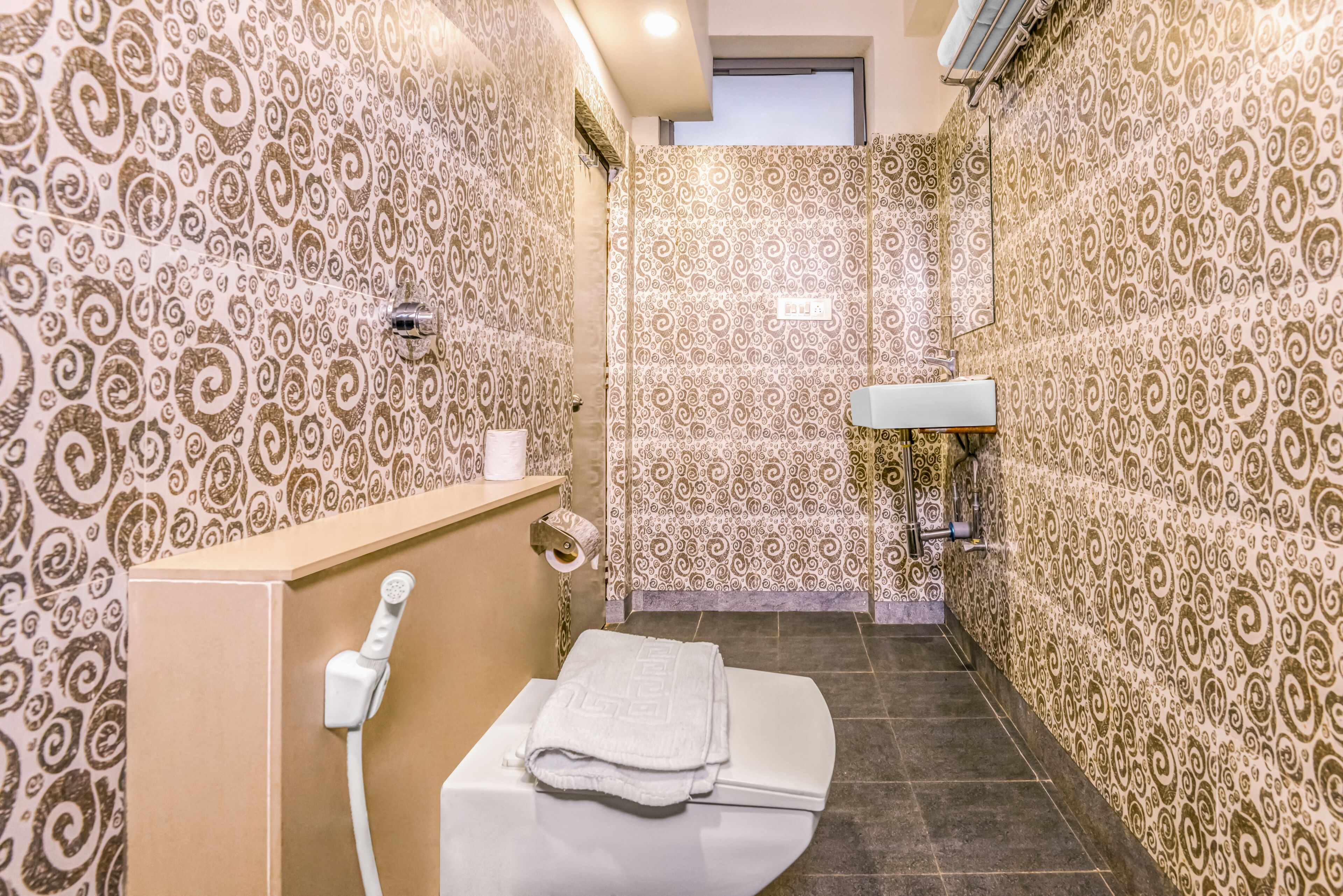 A bathroom with patterned walls, a toilet, a sink, and a shower.