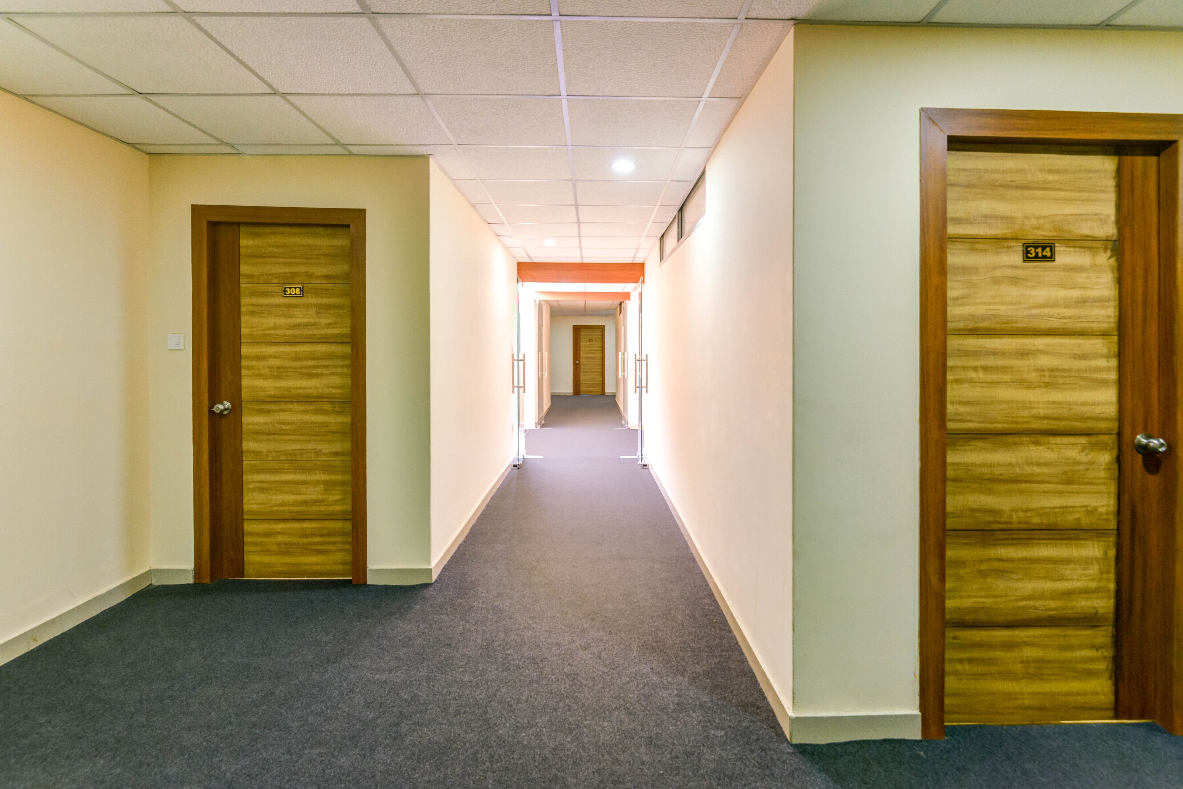 Un couloir doté de revêtements de sol en moquette et de portes en bois, chacune étant munie d’un numéro.