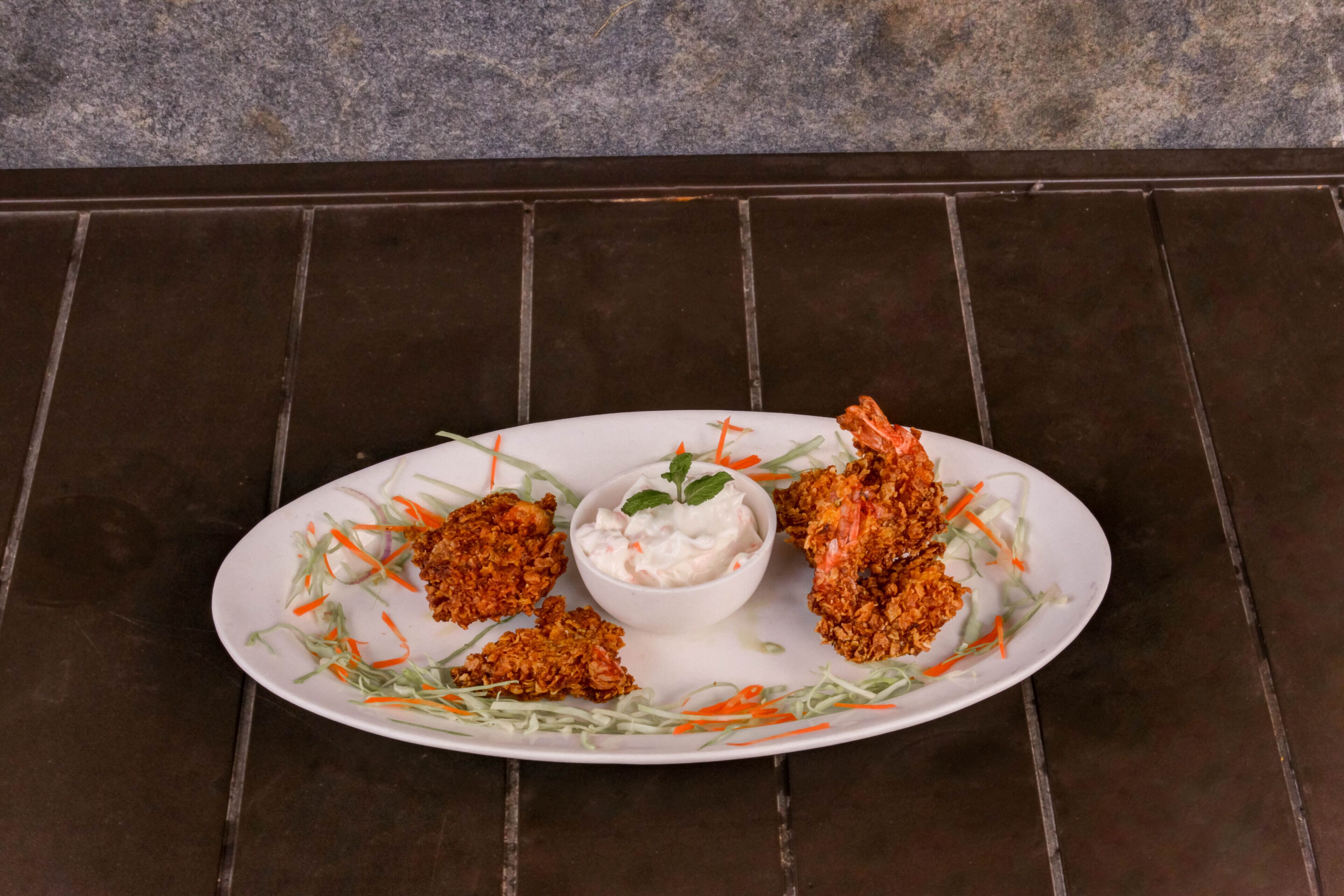 A plate of fried food with a side of coleslaw and a small bowl of sauce.