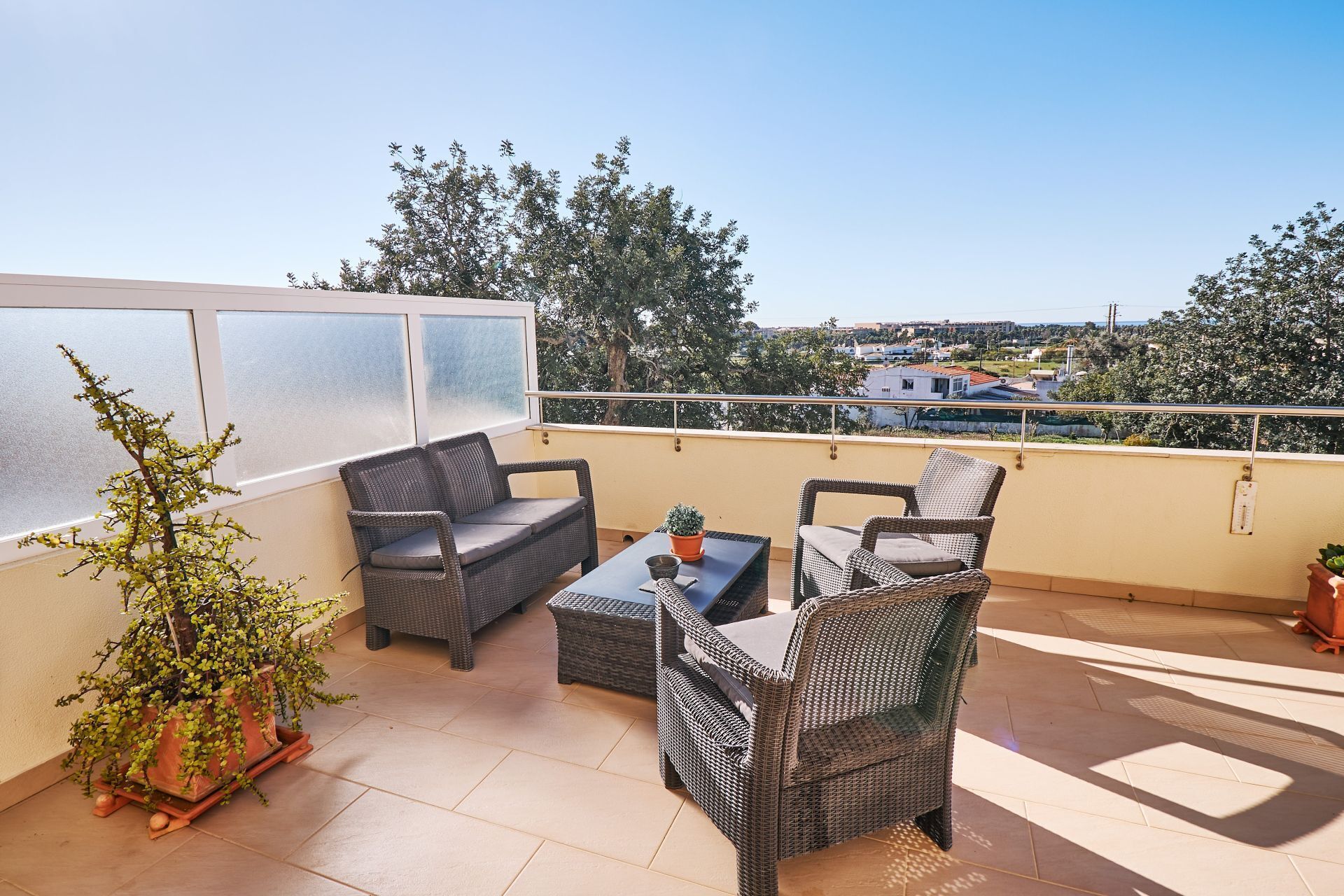 Ein Balkon mit Korbmöbeln, einer Topfpflanze und Blick auf die Stadtlandschaft.