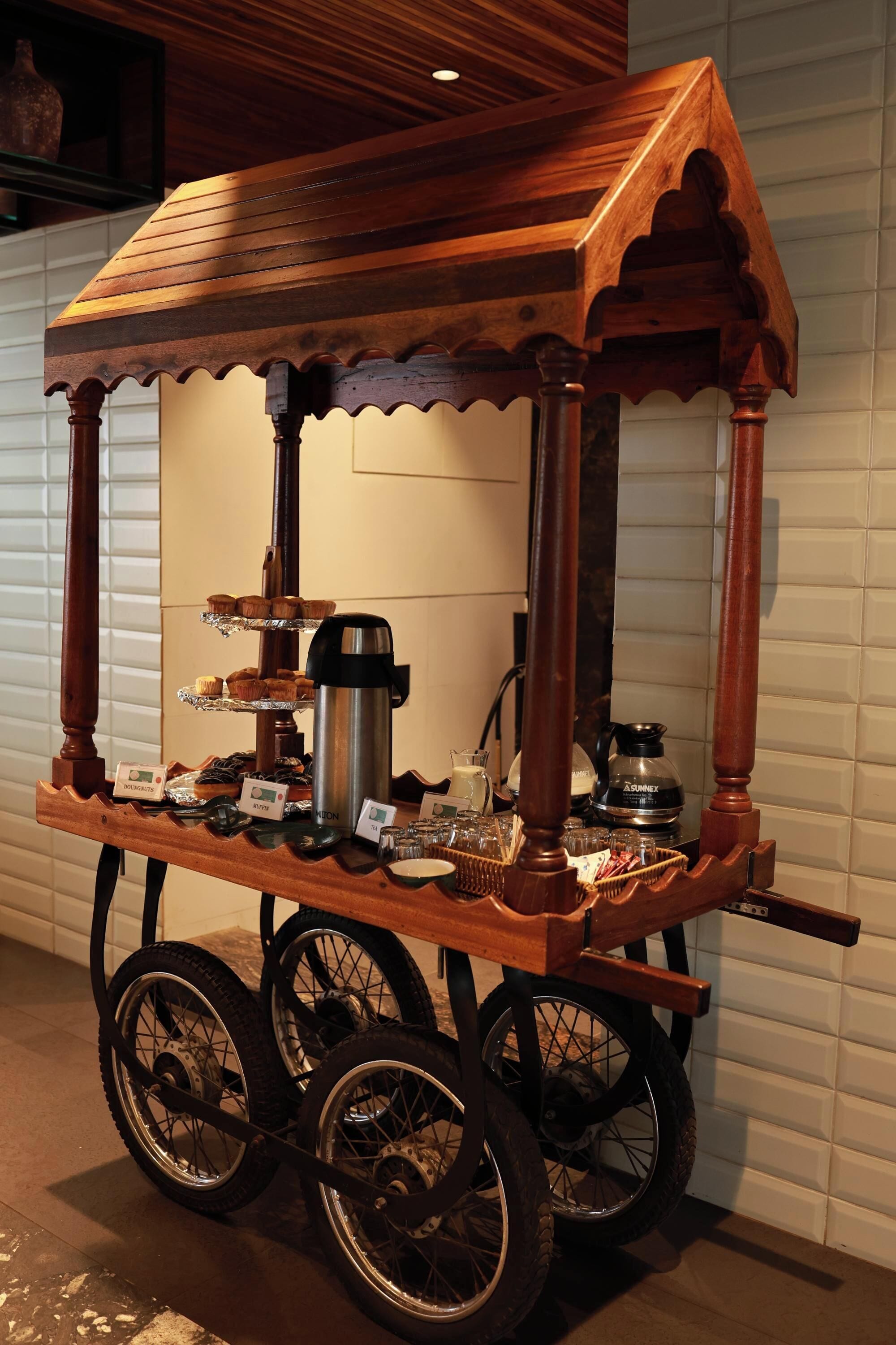 A wooden cart with wheels, a coffee pot, and a tray of muffins.
