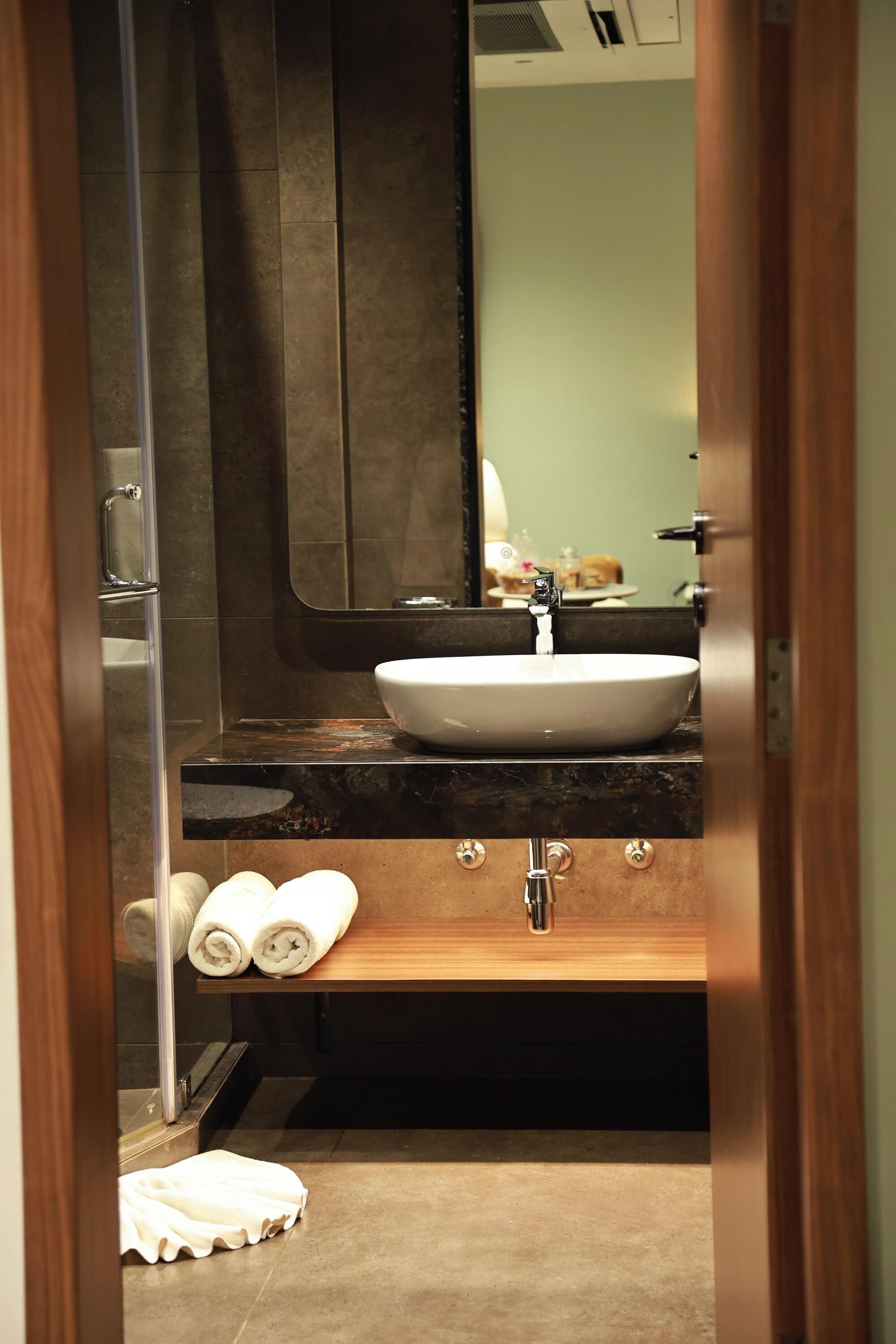 Een badkamer met een wastafel, spiegel, handdoekhouder en douche.