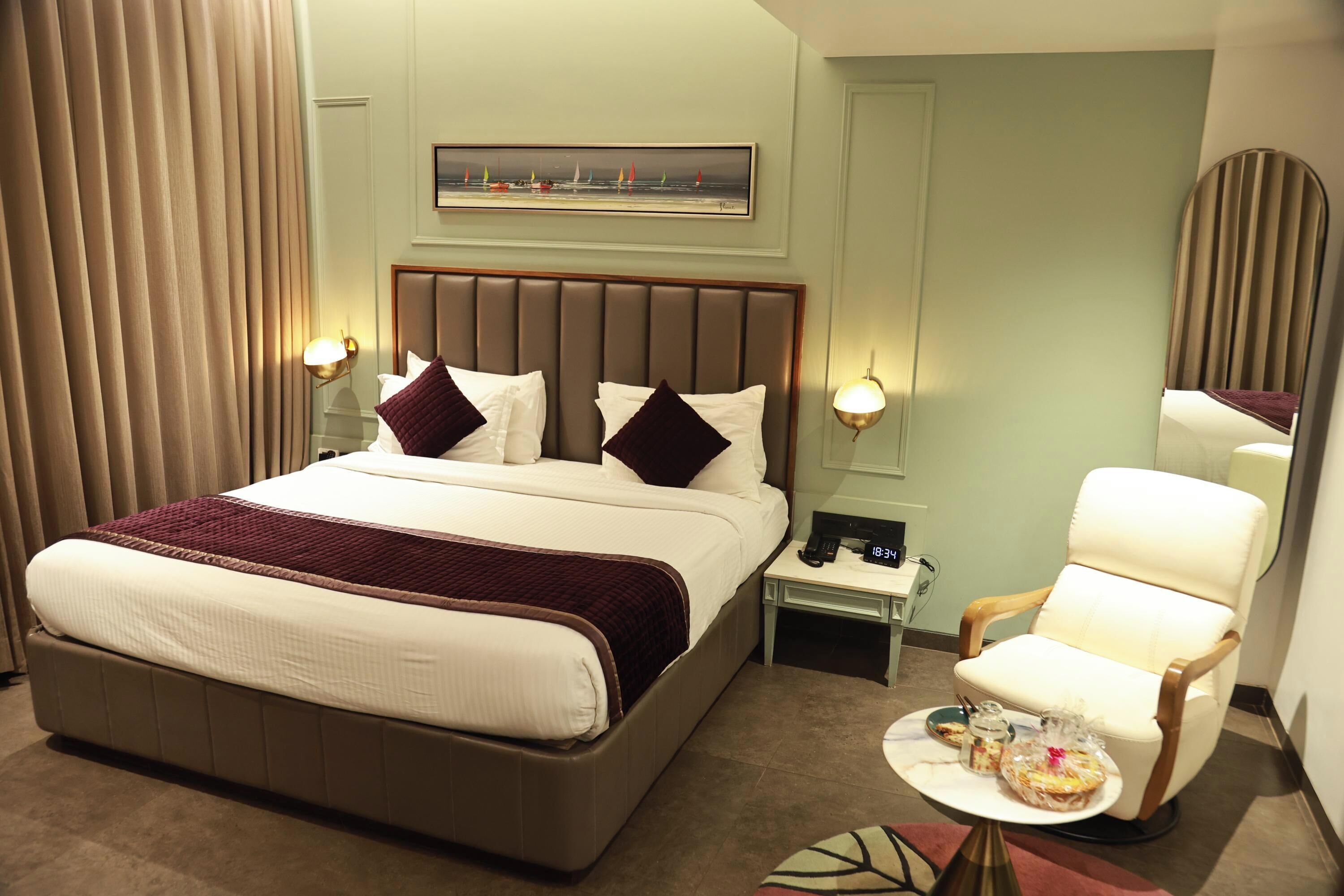 Habitación de hotel con una cama grande, lámparas de noche, una silla, una mesita con una bandeja y un cuadro en la pared.