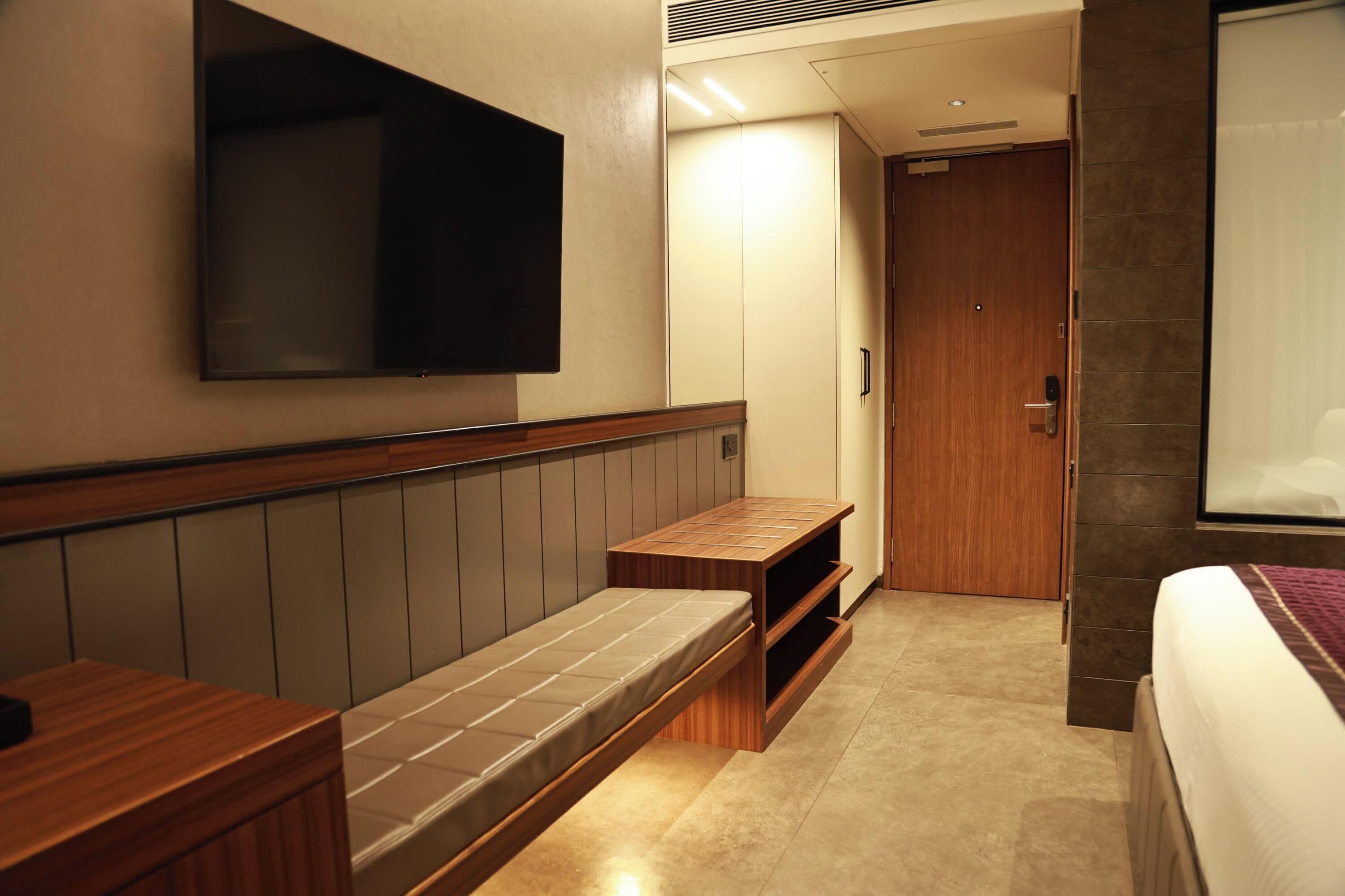 Une chambre d’hôtel avec un lit, un banc, un téléviseur fixé au mur et une porte donnant sur une autre pièce.