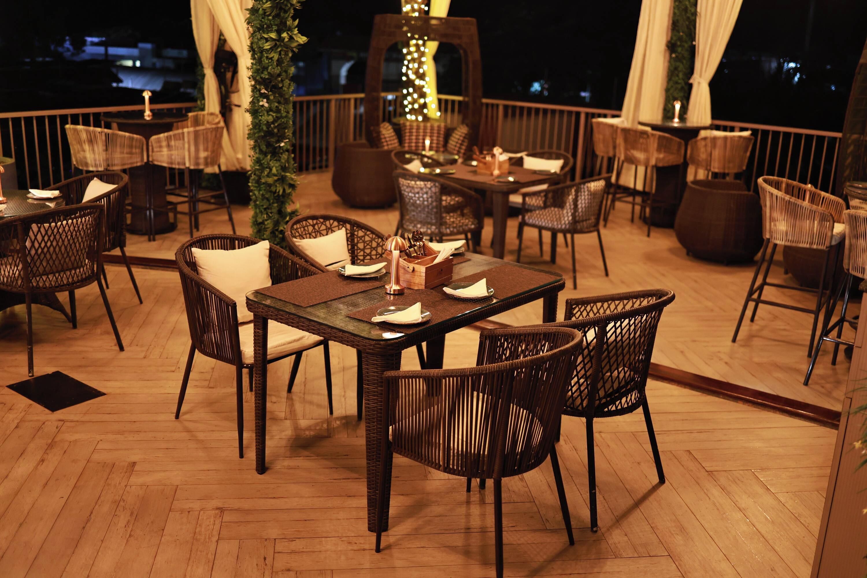 An outdoor dining area with wicker furniture and tables, surrounded by a wooden deck and a railing.