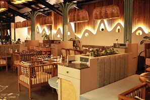 A restaurant interior with wooden furniture, woven light fixtures, and a modern design. - Kamah, Goa (Anjuna)