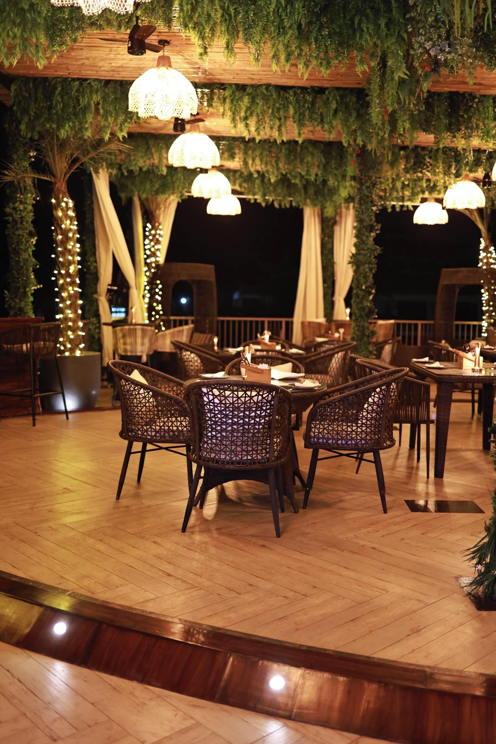 Een terras met rieten meubels, hanglampen en begroeiing.