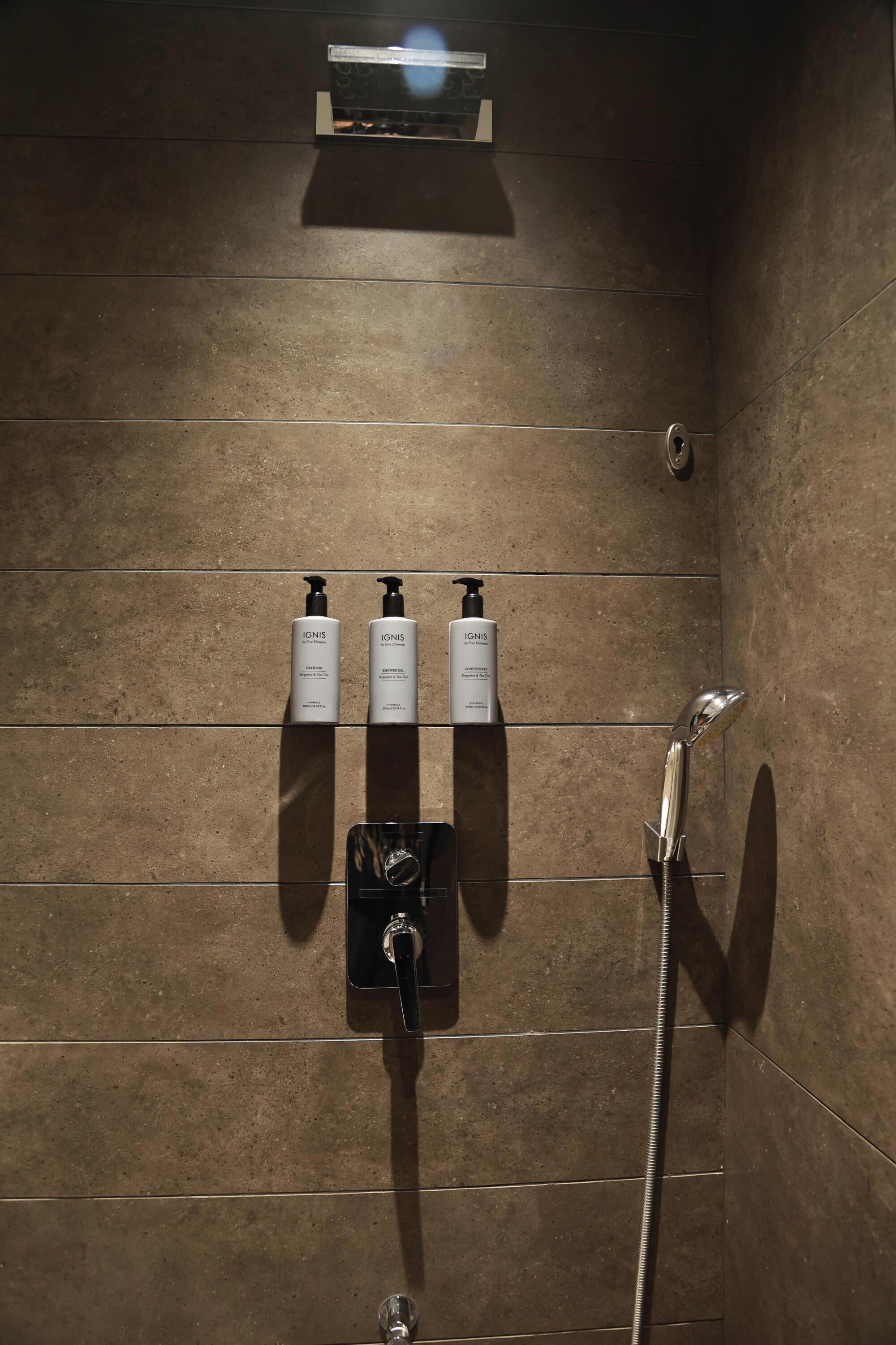 A bathroom with a shower, a hand dryer, and two bottles of shampoo on a shelf.