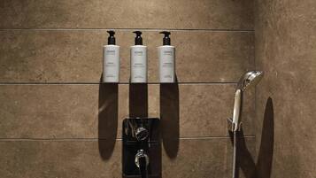 A bathroom with a shower, a hand dryer, and two bottles of shampoo on a shelf.