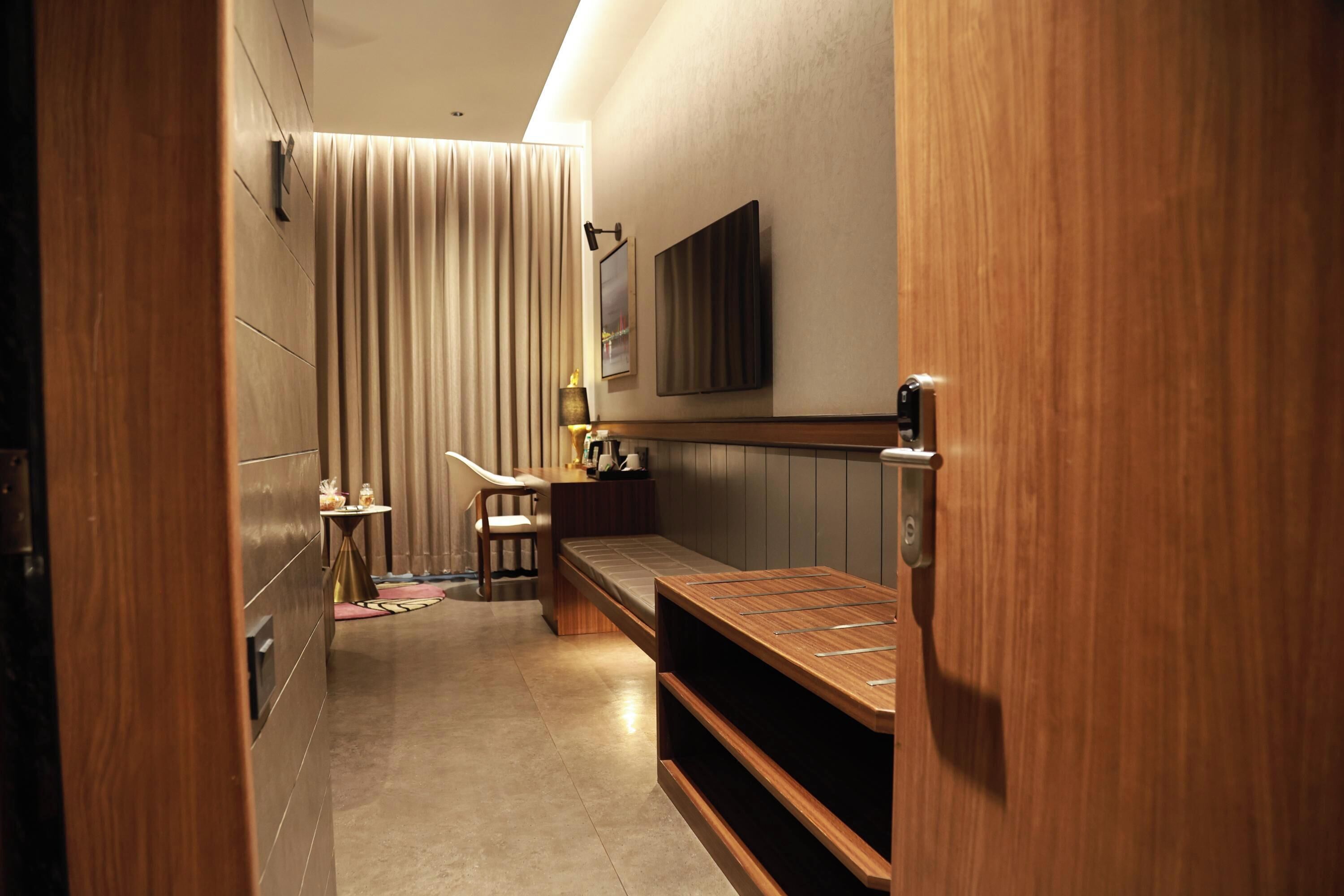 A narrow hallway with a bench, a small table with a lamp, and a television mounted on the wall.