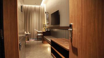 A narrow hallway with a bench, a small table with a lamp, and a television mounted on the wall.