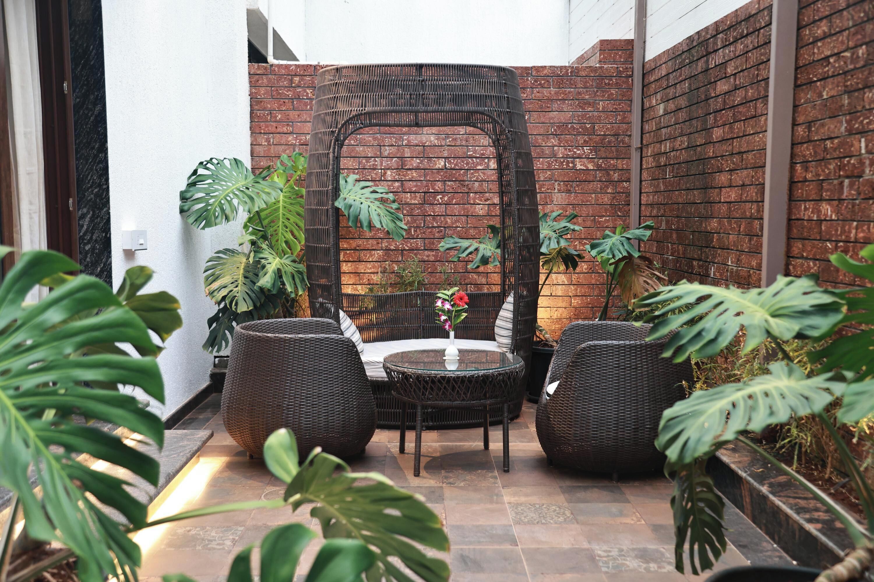 Un patio con mobiliario de mimbre, pared de ladrillo y plantas tropicales.