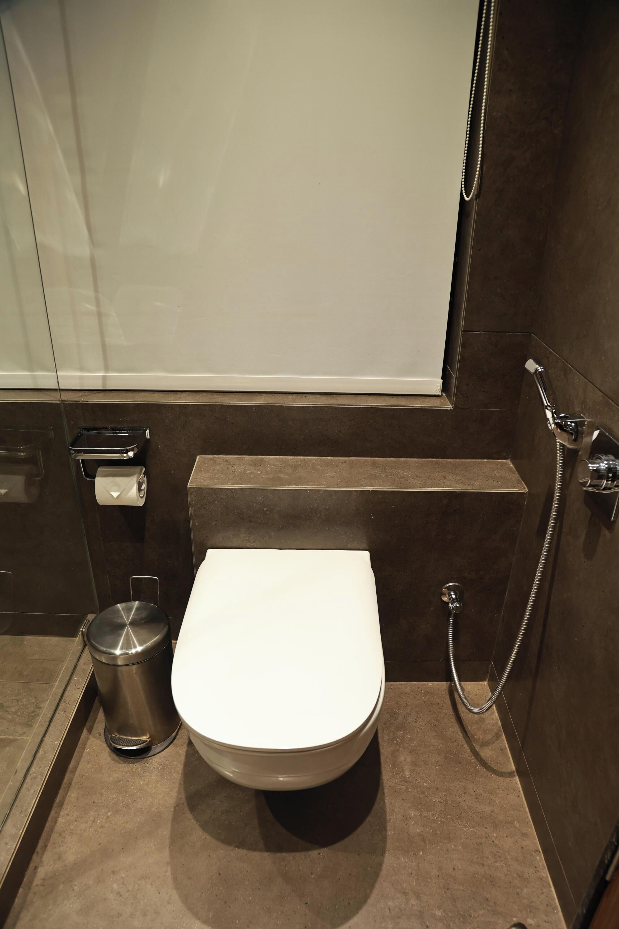 A modern bathroom with a white toilet, a trash bin, and a shower.