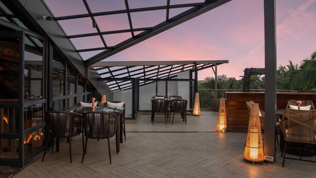 Una terraza en la azotea con paredes de vidrio, suelo de madera y mobiliario exterior.