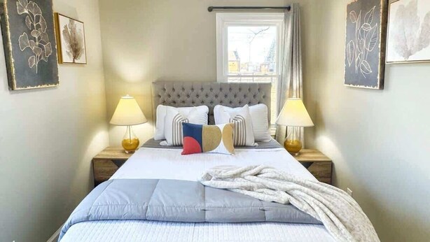 A neatly made bed with a grey headboard, two bedside lamps, and a window with curtains. - Stylish 2BR in Decatur | Big Deck • Pets OK • Quiet Area (Decatur)