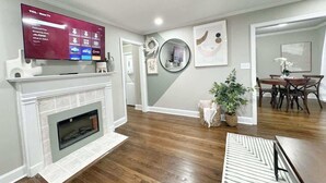 A living room with a fireplace, a mounted TV, and a dining area with a table and chairs. - Stylish 2BR in Decatur | Big Deck • Pets OK • Quiet Area (Decatur)