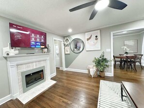 A living room with a fireplace, a mounted TV, and a dining area with a table and chairs.