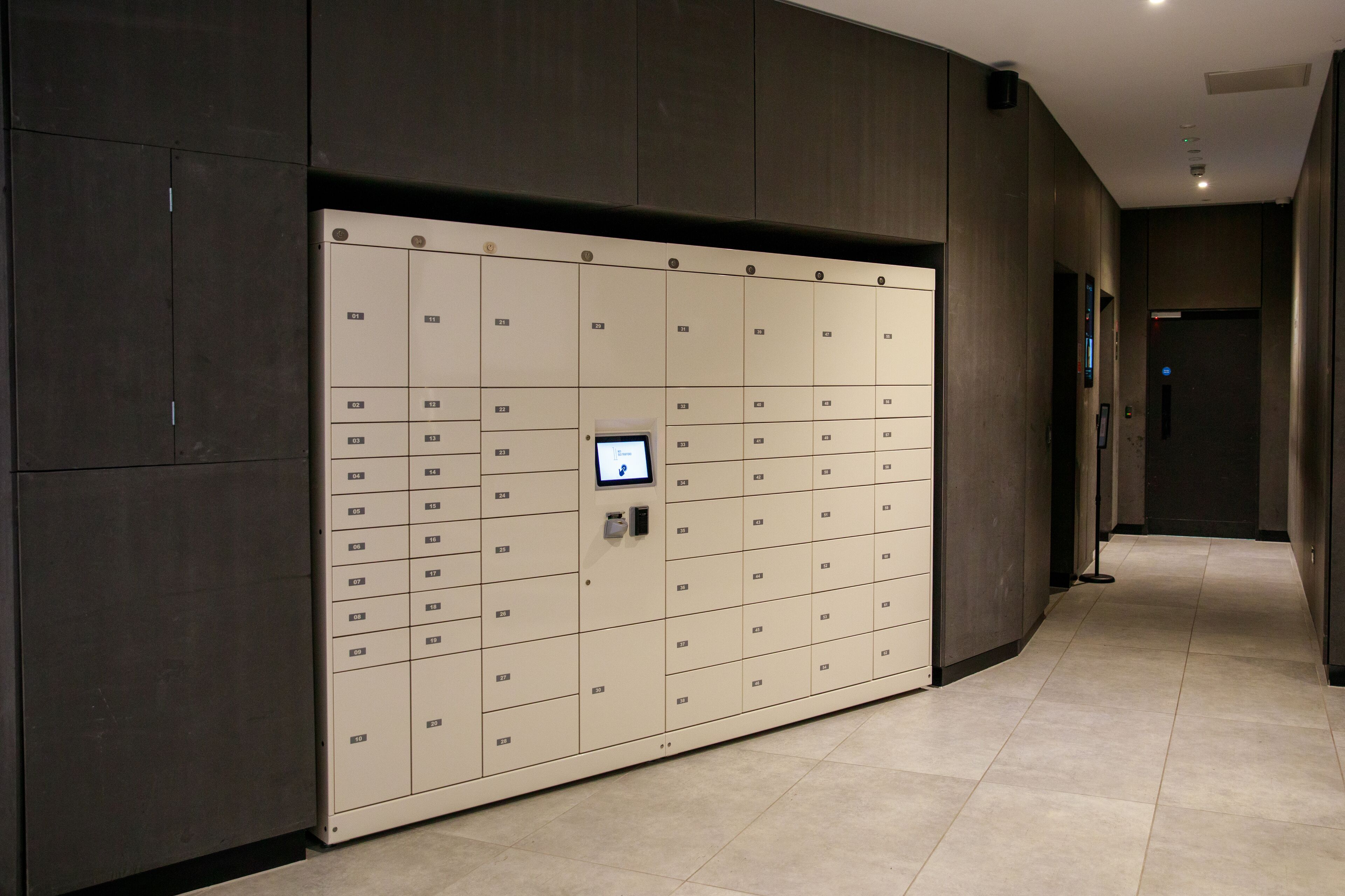 A modern hallway with a row of beige lockers and a digital display.