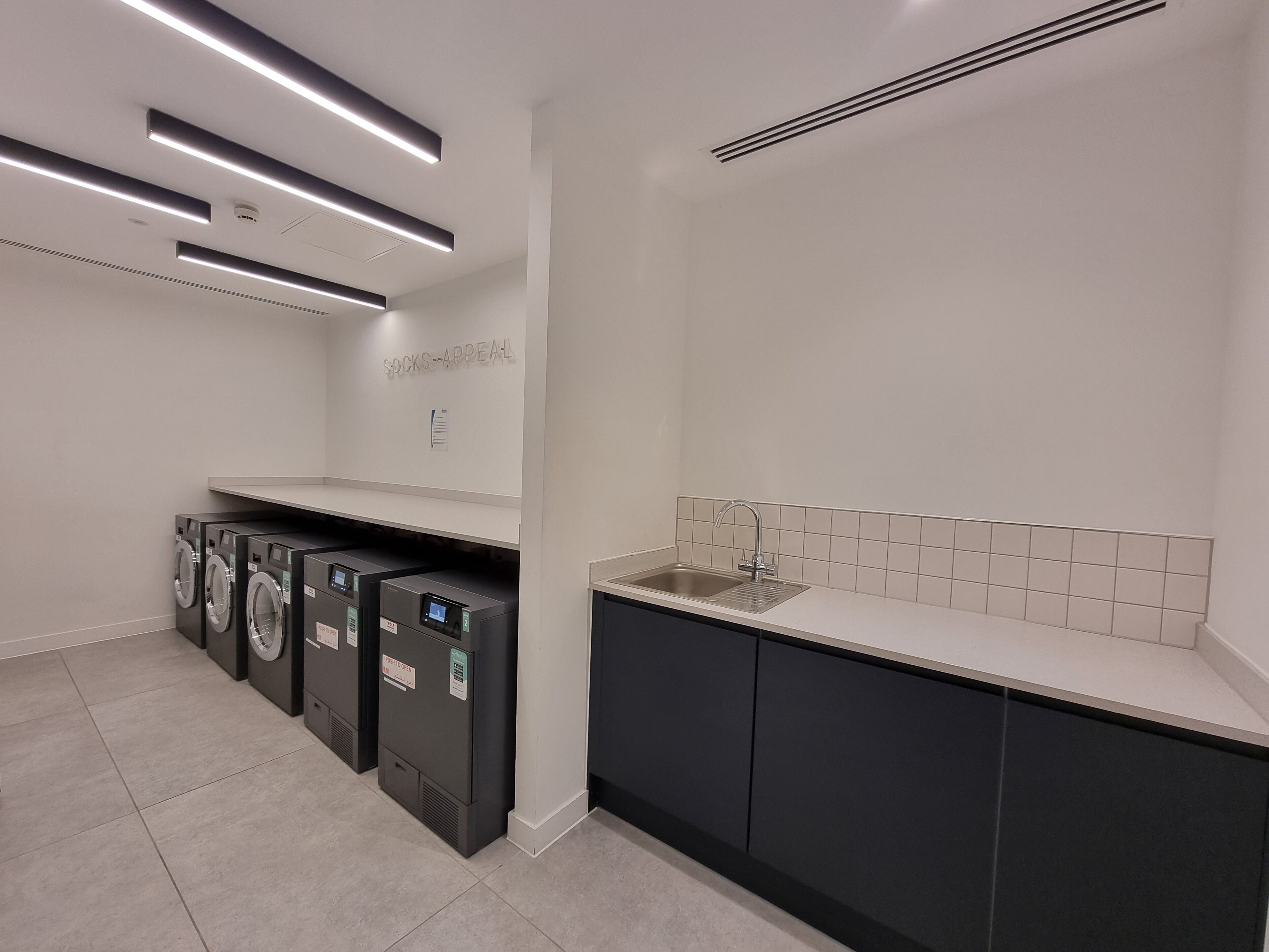A modern laundry facility with multiple washing machines, a sink, and a sign that reads "Socks Appeal".