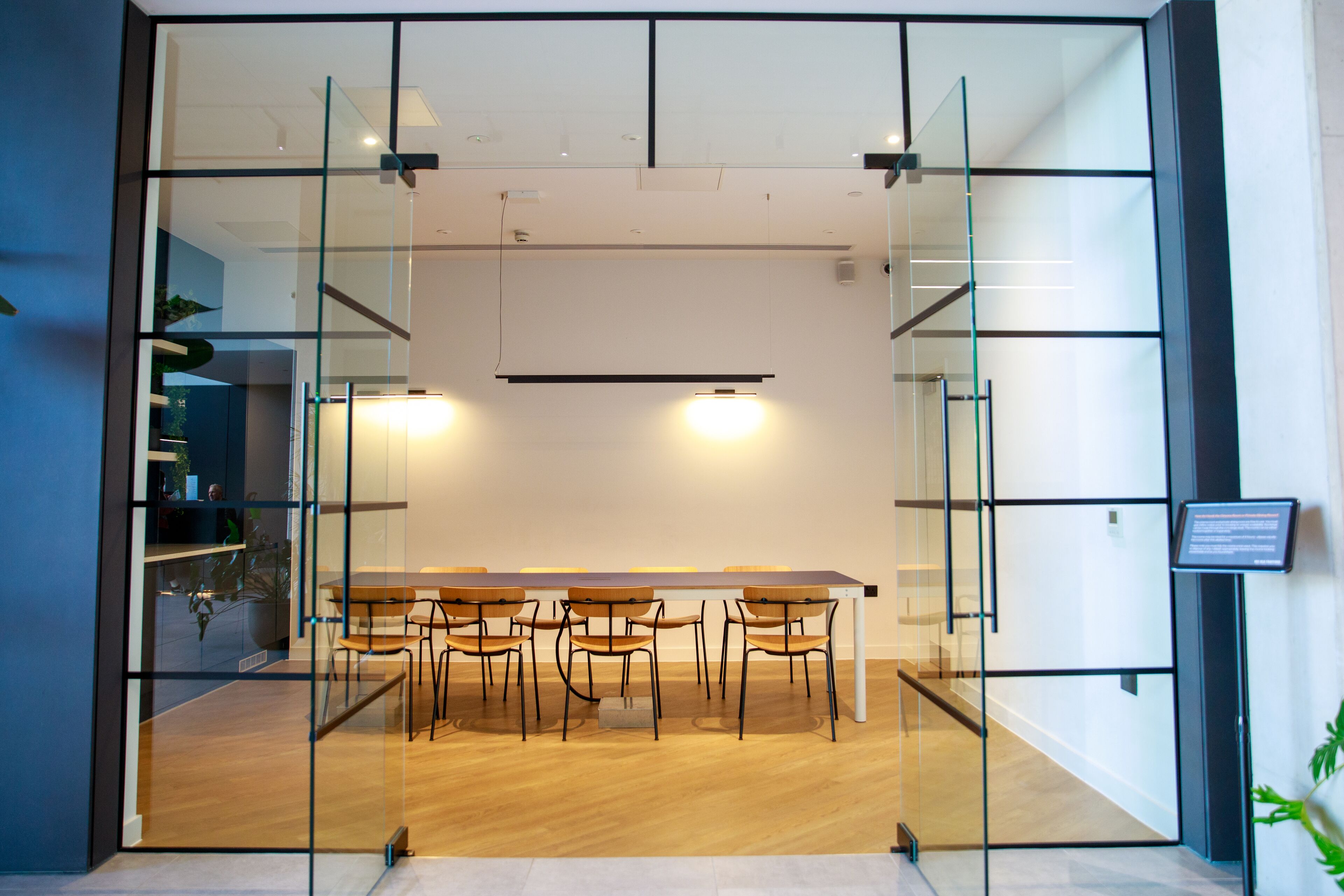A modern meeting room with a glass partition, wooden table, and chairs.