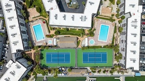 Vue aérienne d’un hôtel doté de deux piscines, de courts de tennis et d’un parking.