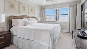 A bedroom with a large bed, a nightstand, a dresser, a ceiling fan, and a window with blinds.