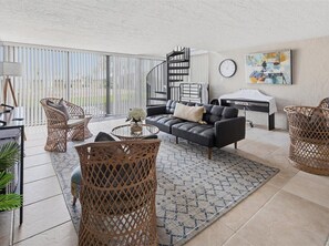 A living room with a sofa, wicker chairs, a coffee table, a spiral staircase, a clock, and a painting on the wall.