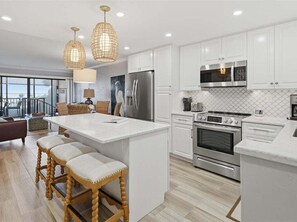 A modern kitchen with white cabinetry, stainless steel appliances, and a central island with bar stools.