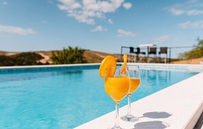 Une vue sur la piscine avec deux verres d’une boisson à l’orange, un ciel dégagé et un paysage lointain.