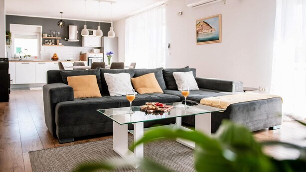 A modern living room with a dark grey sofa, a glass coffee table, and a kitchen in the background. - Stunning home in Sibenik (Sibenik)