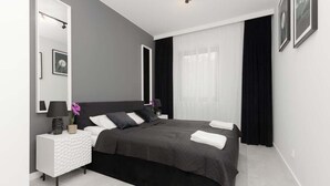 Un dormitorio moderno con una cama grande, una mesita de noche, un espejo y una ventana con cortinas.