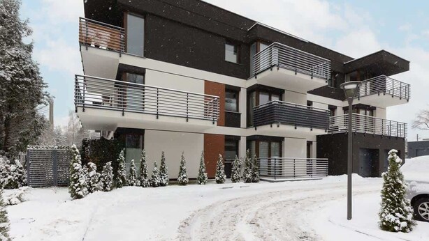 Un edificio moderno de varios pisos con balcones, una entrada protegida por una reja y alrededores cubiertos de nieve.