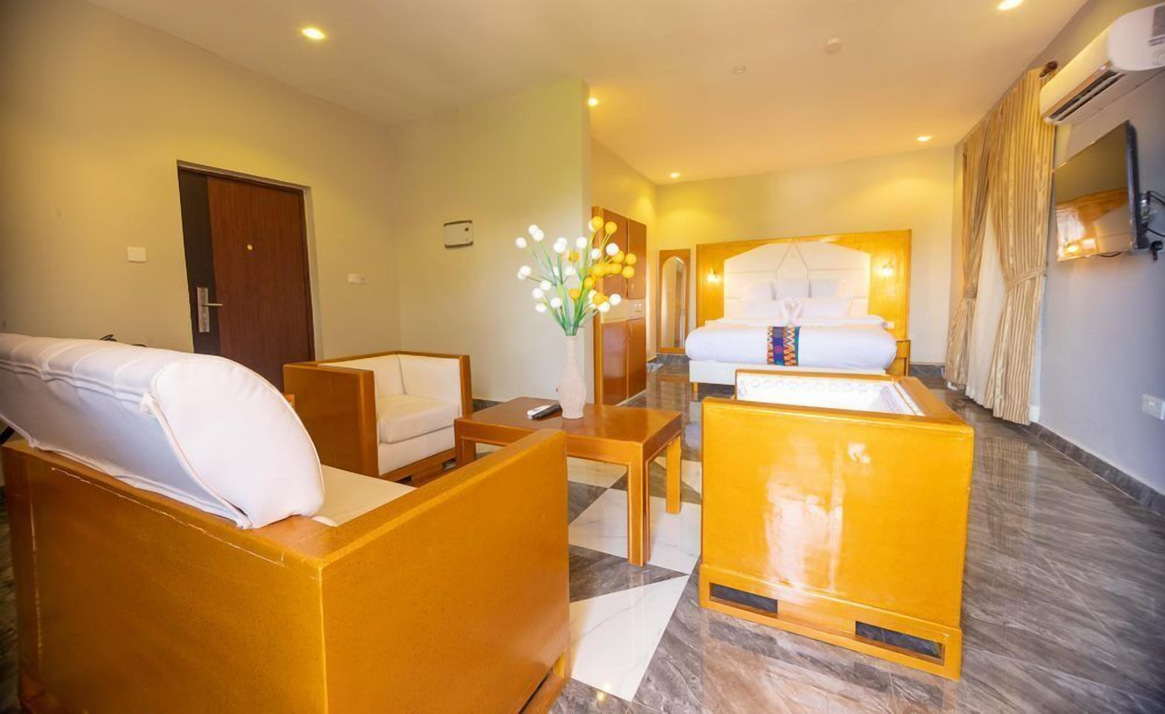 Habitación de hotel con cama, sofá, sillón, una mesita y un jarrón con flores.