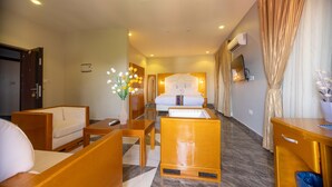 Een hotelkamer met een bed, een bureau, een stoel, een klein tafeltje, een vaas met bloemen en een televisie aan de muur.