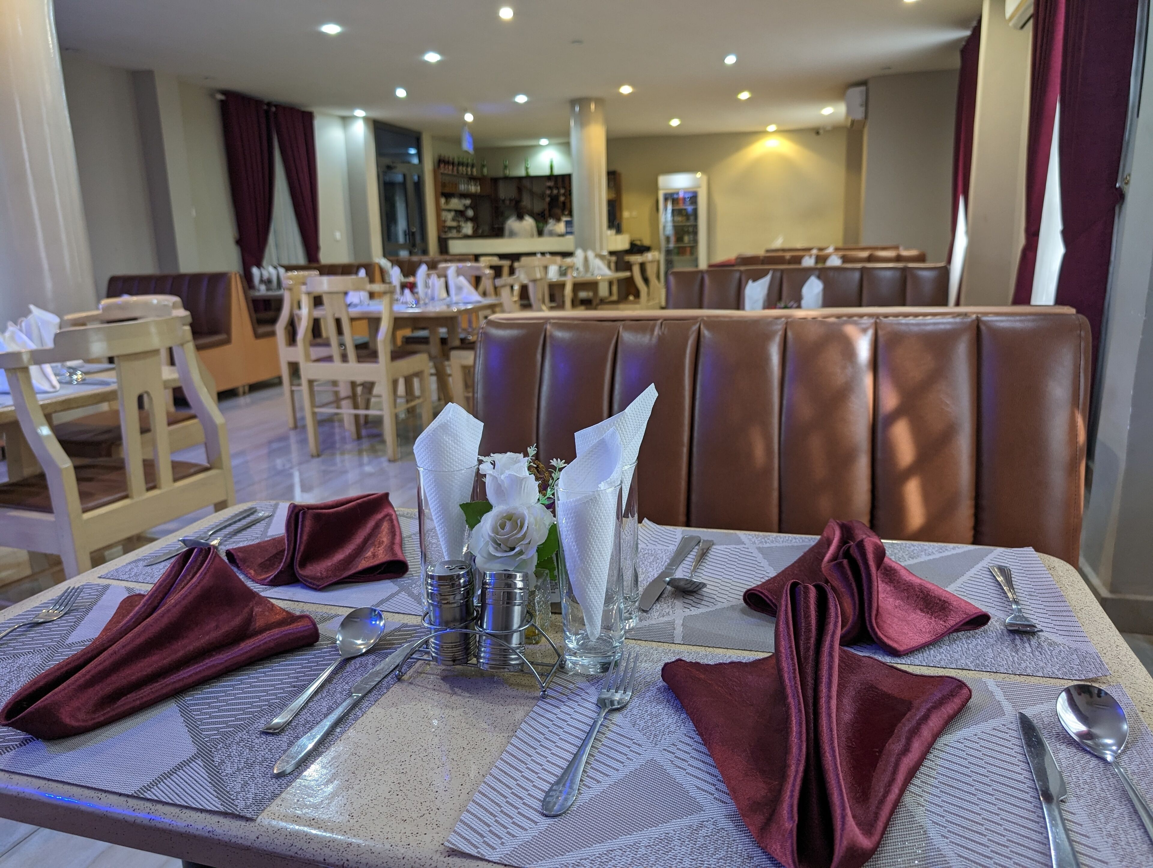 Comedor con mesas dispuestas para dos, mantel de mármol, servilletas rojas y cubertería.