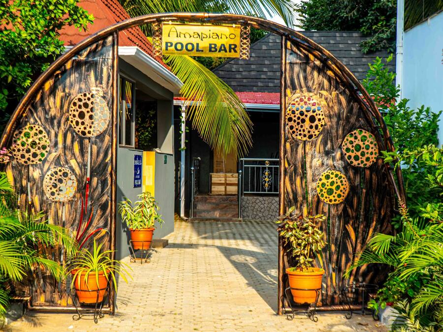 A pool bar entrance with a sign, surrounded by potted plants and a rustic wooden archway.
