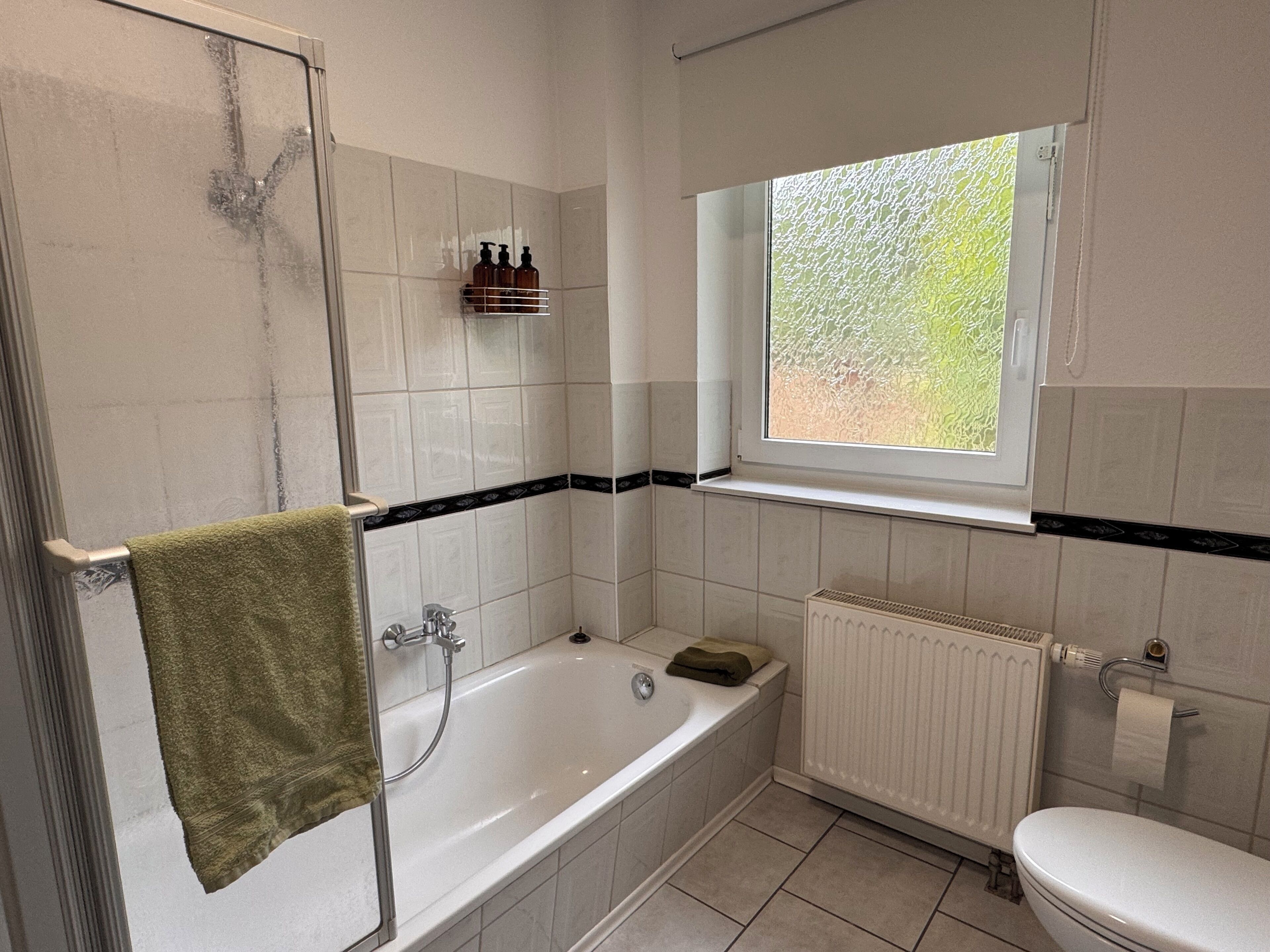 A bathroom with a bathtub, a toilet, a window, and a shower.