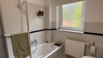 A bathroom with a bathtub, a toilet, a window, and a shower.