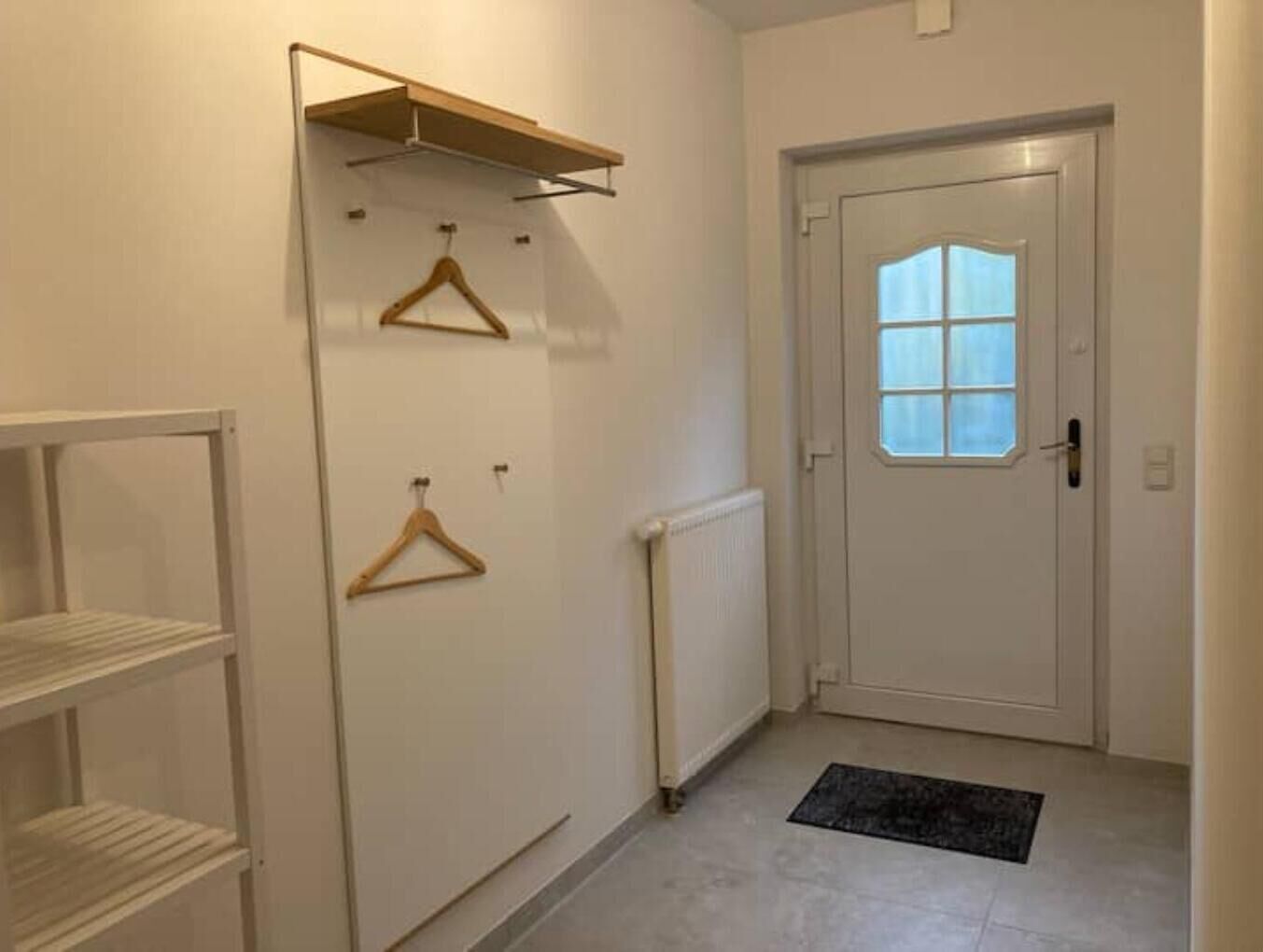 A hallway with a white door, a radiator, and wooden hangers on the wall.