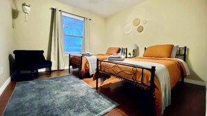 A bedroom with a bed, a chair, a window with curtains, and a rug. - Blue Jay's Magnolia - 3BR 2BA - Family Friendly (Lubbock)