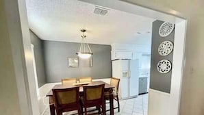 A dining area with a table and chairs, a ceiling light, and a refrigerator in the background. - Blue Jay's Magnolia - 3BR 2BA - Family Friendly (Lubbock)