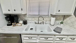 A kitchen with white cabinets, a double sink, a coffee maker, and a small plant. - Blue Jay's Magnolia - 3BR 2BA - Family Friendly (Lubbock)