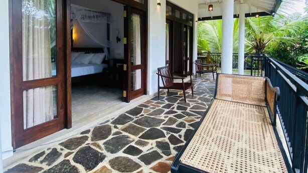 A covered outdoor area with a stone floor, wooden furniture, and a bed visible through an open door. - White Villa (Tangalle)