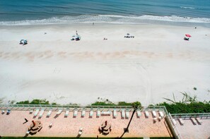 A beach with sun loungers and umbrellas, a pool area with lounge chairs, and a view of the ocean.