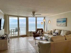 A living room with a sofa, armchairs, a coffee table, and a view of the ocean through large sliding doors.