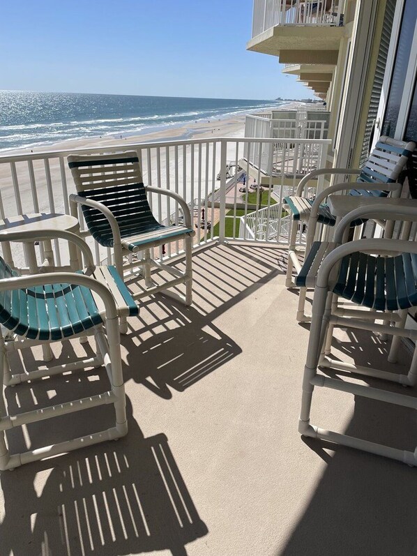 A balcony with chairs and a table overlooking the beach.